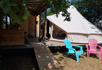 Lodge Sybley Apex tent al Campeggio Junora in Francia con terrazza in legno e sedie colorate all’esterno.
