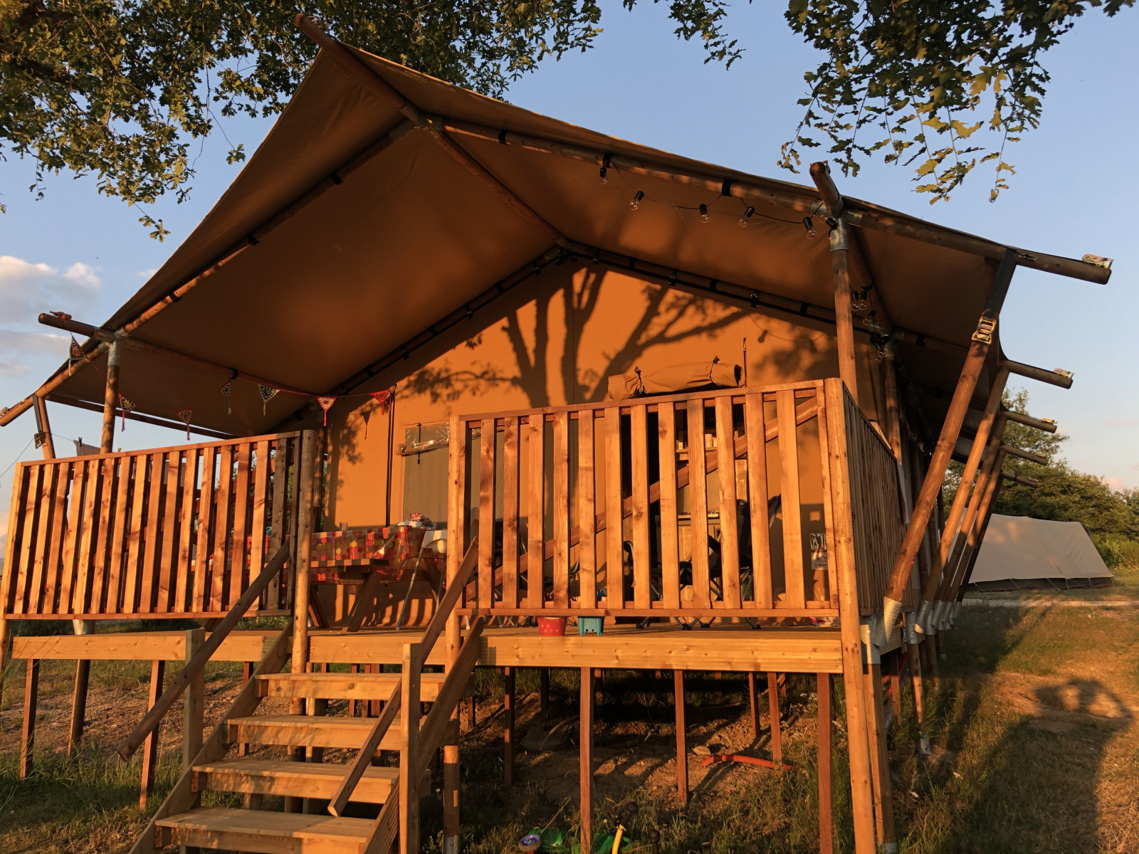 Luxe en ruim eco-lodge safaritent zonovergoten met houten terras en balustrade in de natuur.
