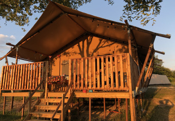 Tenda safari eco-lodge di lusso e spaziosa illuminata dal sole con veranda e balaustra in legno.
