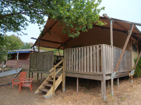 Tente safari Eco-lodge luxueuse et spacieuse au camping Junora en France, terrasse en bois et chaises devant.