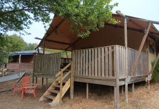 Tenda safari eco-lodge di lusso e spaziosa al Camping Junora in Francia, con veranda in legno e sedie.