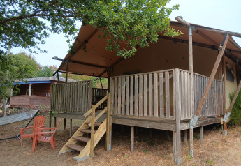 Tenda safari eco-lodge di lusso e spaziosa al Camping Junora in Francia, con veranda in legno e sedie.