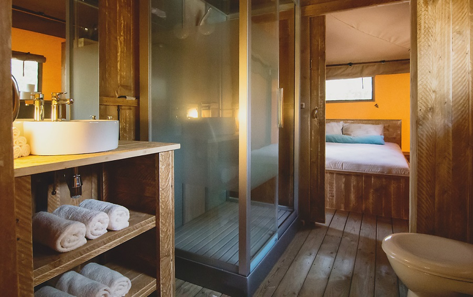 Luxe en ruim safari tent badkamer met houten interieur, douchecabine en uitzicht op slaapkamer.