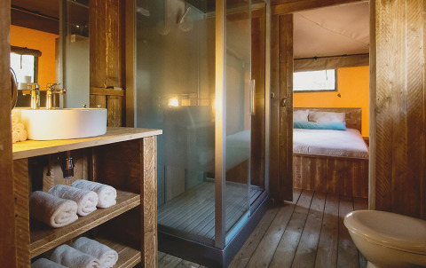 Bagno di tenda safari lussuosa e spaziosa con interni in legno, doccia e vista sulla camera da letto.