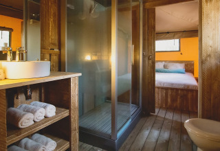 Bagno di tenda safari lussuosa e spaziosa con interni in legno, doccia e vista sulla camera da letto.