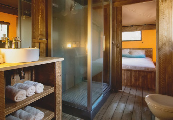 Bagno di tenda safari lussuosa e spaziosa con interni in legno, doccia e vista sulla camera da letto.