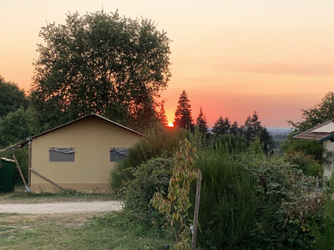 Tramonto dietro gli alberi presso la tenda safari di lusso al Campeggio Junora, immersa nel verde in Francia.