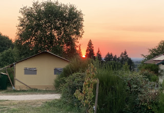 Coucher de soleil derrière les arbres près d'une tente safari luxueuse au Camping Junora, entouré de verdure.