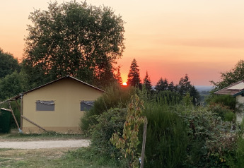 Atardecer tras árboles junto a una lujosa tienda safari en el Camping Junora, rodeado de naturaleza en Francia.