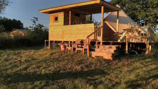 Solbeskinnet Bell XL familieteltlodge med træterrasse og udendørs siddepladser i landlige omgivelser.