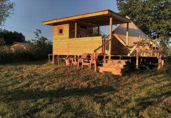 Bell XL family tent lodge featuring a wooden deck and outdoor chairs, bathed in warm evening sunlight.