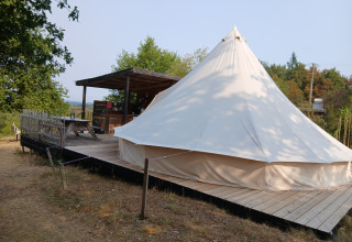 Tente familiale Bell XL au camping Junora en France, avec terrasse en bois et coin salon extérieur couvert.