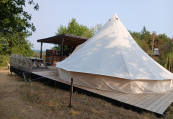 Tente familiale Bell XL au camping Junora en France, avec terrasse en bois et coin salon extérieur couvert.