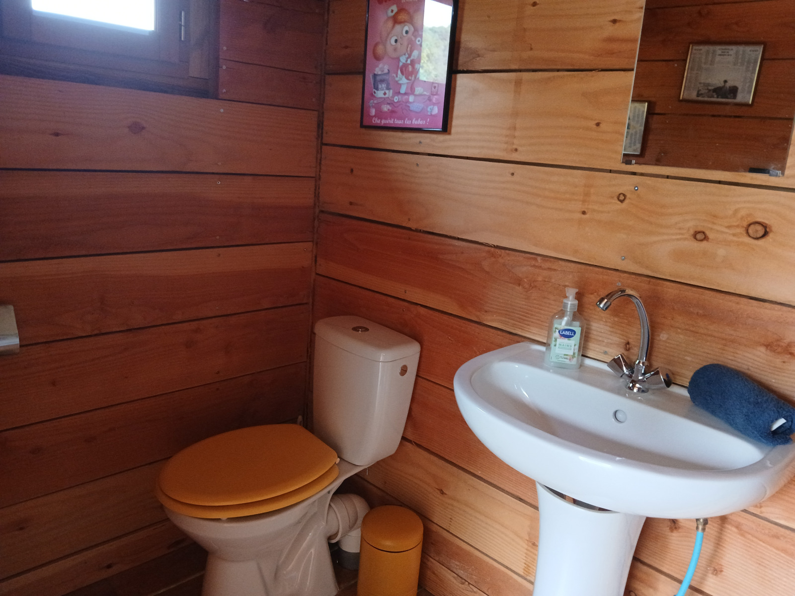 Houten badkamer met gele wc-bril, wastafel en spiegel in Bell XL family tent op Camping Junora in Frankrijk.