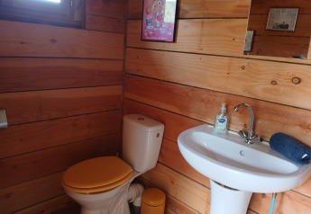 Wood-paneled bathroom with yellow toilet seat, sink, and mirror in Bell XL family tent at Campsite Junora.