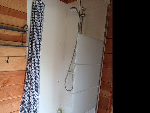 Douche avec cloison vitrée et rideau à motifs dans la tente familiale Bell XL au Camping Junora, France.