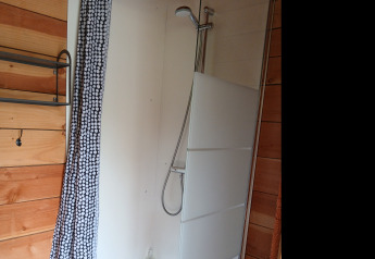 Douche avec cloison vitrée et rideau à motifs dans la tente familiale Bell XL au Camping Junora, France.