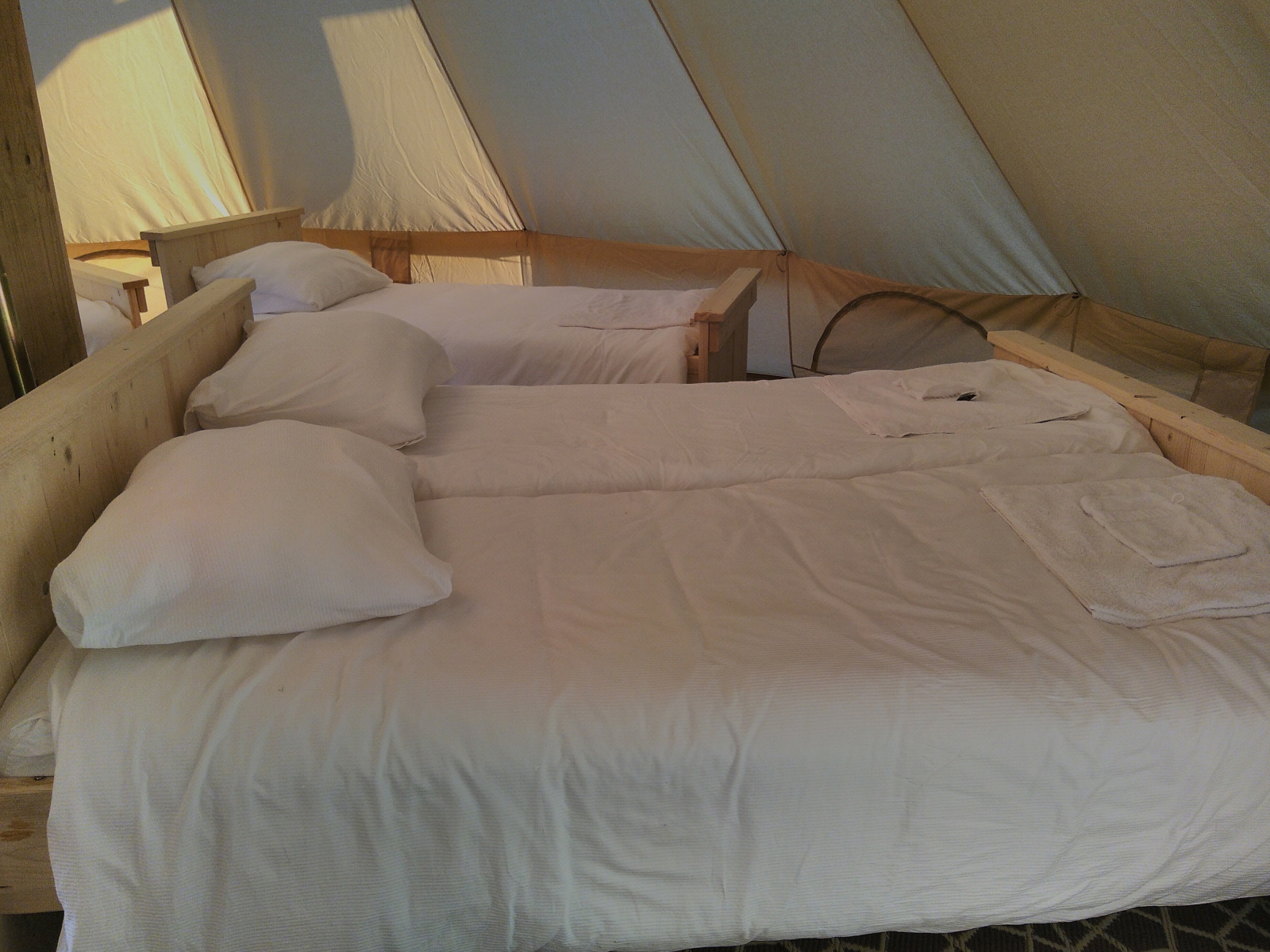 Binnen in de Bell XL familietent op Campsite Junora in Frankrijk met drie opgemaakte bedden en wit linnengoed.