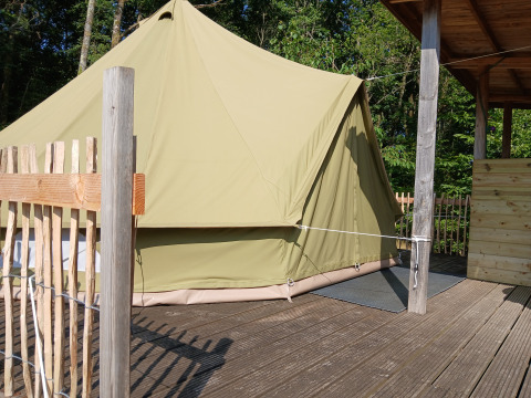 Stor beige bell-telt på træterrasse ved Campsite Junora i Frankrig, omgivet af skov og hegn.