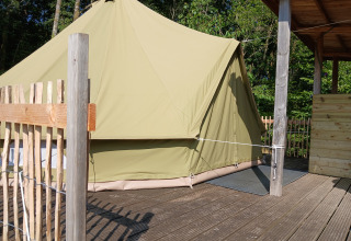 Stor beige bell-telt på træterrasse ved Campsite Junora i Frankrig, omgivet af skov og hegn.