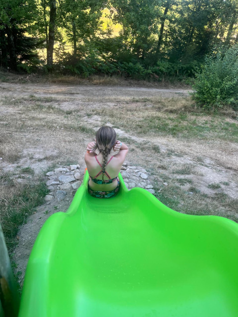 Een kind zit aan het eind van een groene glijbaan bij Bell tent «6M» op Campsite Junora in Frankrijk.