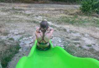 Un bambino è seduto alla fine di uno scivolo verde presso Bell tent «6M» al Campeggio Junora in Francia.