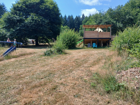 Vista della Bell tent «6M» al Campeggio Junora in Francia, prato verde, rifugio in legno e bambini che giocano.