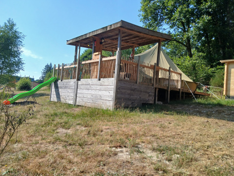 Bell tent med træterrasse, grøn rutsjebane og omgivet af træer på Campsite Junora i Frankrig