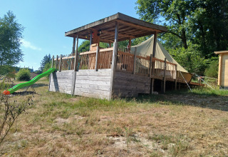 Tienda Bell con terraza de madera y tobogán verde en el Camping Junora, Francia, rodeada de árboles