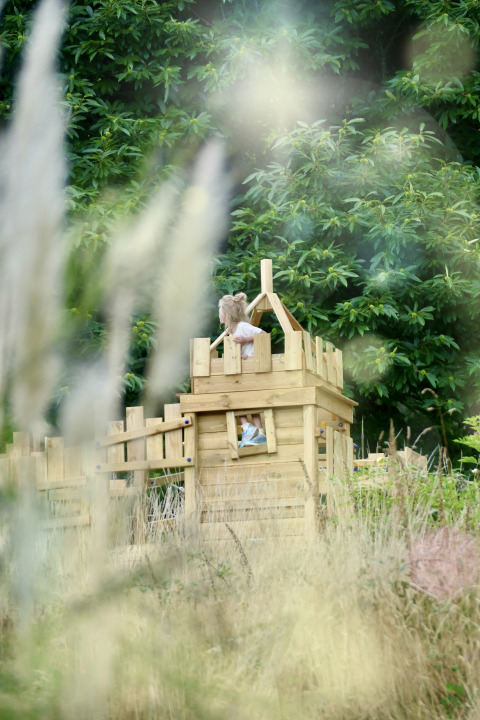 Un niño juega en una casa de madera en Bell tent «6M» en el Camping Junora en Francia, rodeado de vegetación.