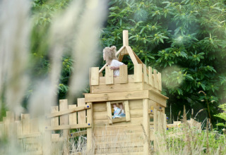Un niño juega en una casa de madera en Bell tent «6M» en el Camping Junora en Francia, rodeado de vegetación.