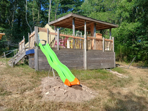 Toboggan vert près d'une terrasse en bois et d'une tente au camping Junora, en France, entouré de nature.