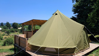 Large bell tent set on a wooden platform with covered patio, surrounded by greenery under a clear sky.