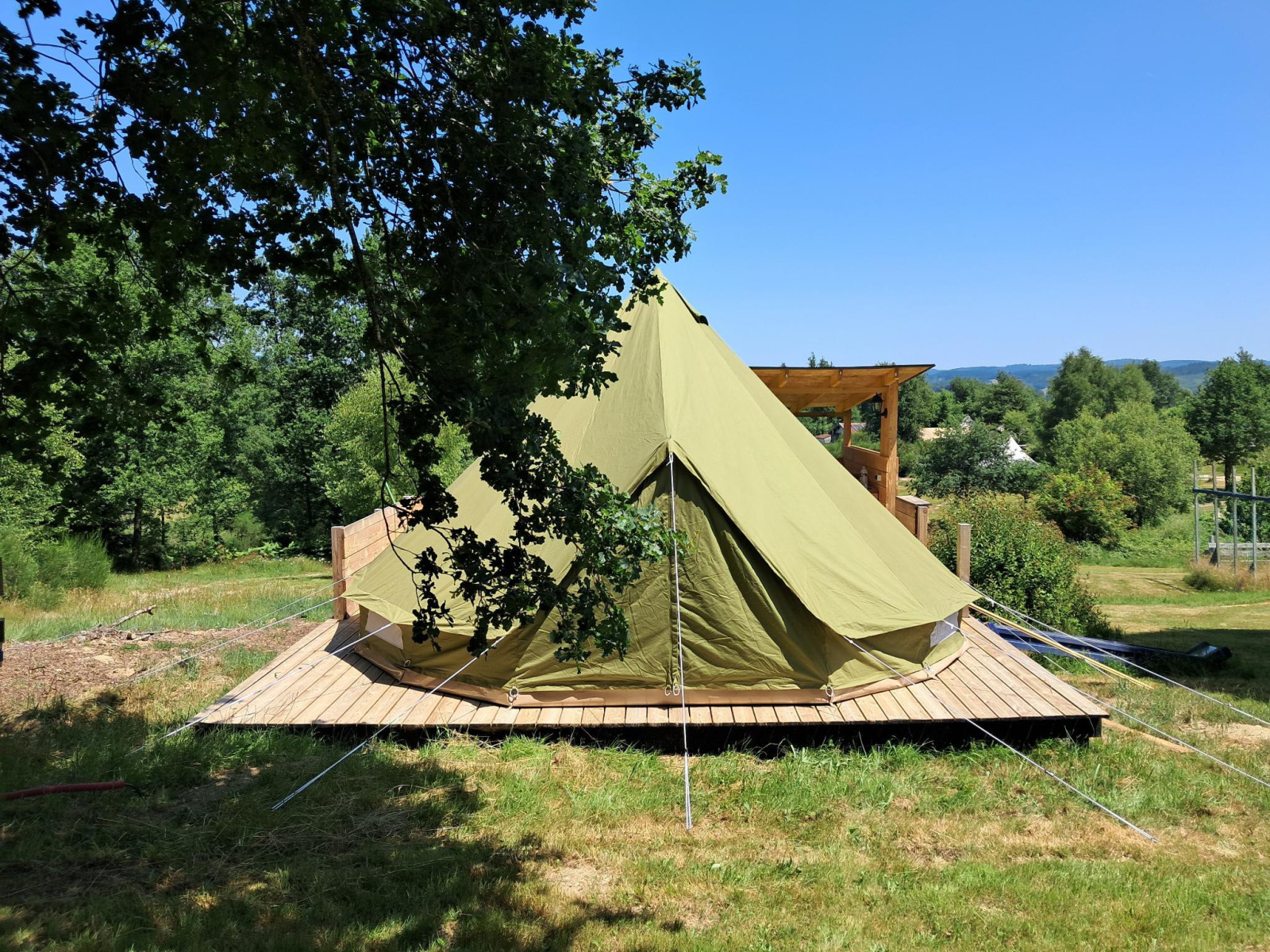 Grote bell tent op een houten platform bij Campsite Junora in Frankrijk, omgeven door groene bomen en velden.