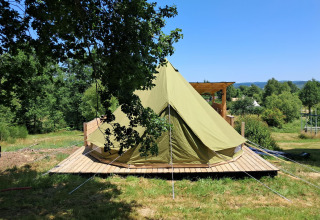 Grande tenda campana su piattaforma in legno al Campeggio Junora, Francia, circondata dal verde e cielo sereno.