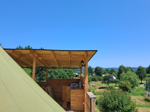 Vista dalla terrazza in legno della Bell tent «6M» al Campeggio Junora in Francia, con alberi e campi verdi.
