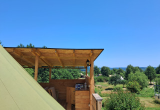 Vista desde una terraza de madera en la tienda Bell tent «6M» en el Camping Junora, Francia, con campo y árboles.