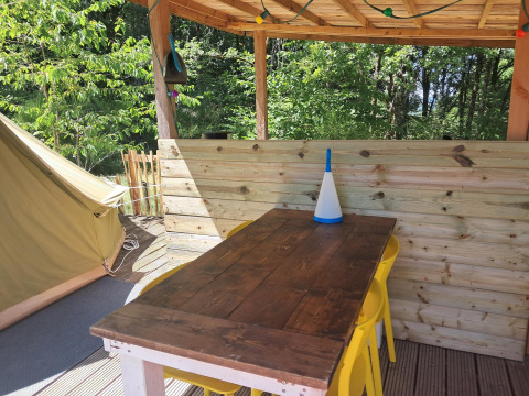 Udendørs spiseområde med træbord, gule stole og telt ved Bell tent «6M» på Campsite Junora, Frankrig.