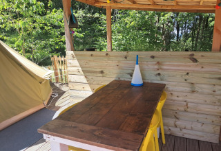 Udendørs spiseområde med træbord, gule stole og telt ved Bell tent «6M» på Campsite Junora, Frankrig.