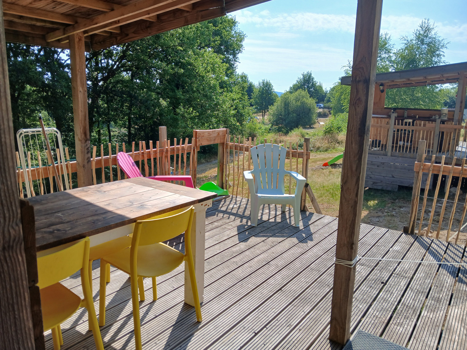 Houten terras met kleurrijke stoelen bij Bell tent 6M op Camping Junora in Frankrijk, uitzicht op de natuur.