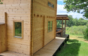 Wooden lodge named Avignon at Campsite Junora in France, surrounded by lush greenery and blue sky.