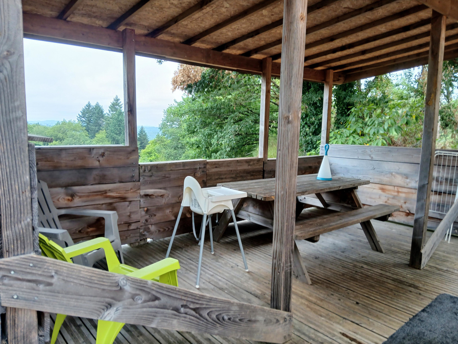 Overdekt houten terras met picknickbank en stoelen bij lodge 'Avignon' op Camping Junora in Frankrijk.