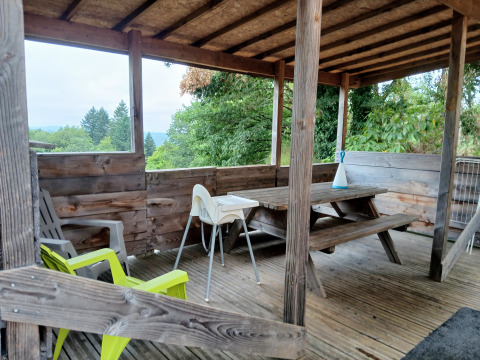 Overdekt houten terras met picknickbank en stoelen bij lodge 'Avignon' op Camping Junora in Frankrijk.