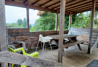 Overdekt houten terras met picknickbank en stoelen bij lodge 'Avignon' op Camping Junora in Frankrijk.