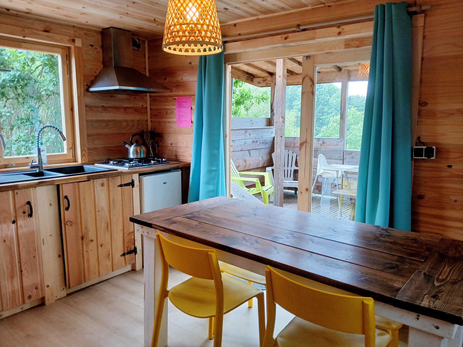 Houten lodge-keuken met gele stoelen, eettafel, terras en natuurzicht op Campsite Junora bij Avignon.