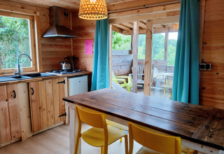 Cucina di un lodge in legno con sedie gialle, tavolo, terrazza e vista natura al Campsite Junora, Avignon.