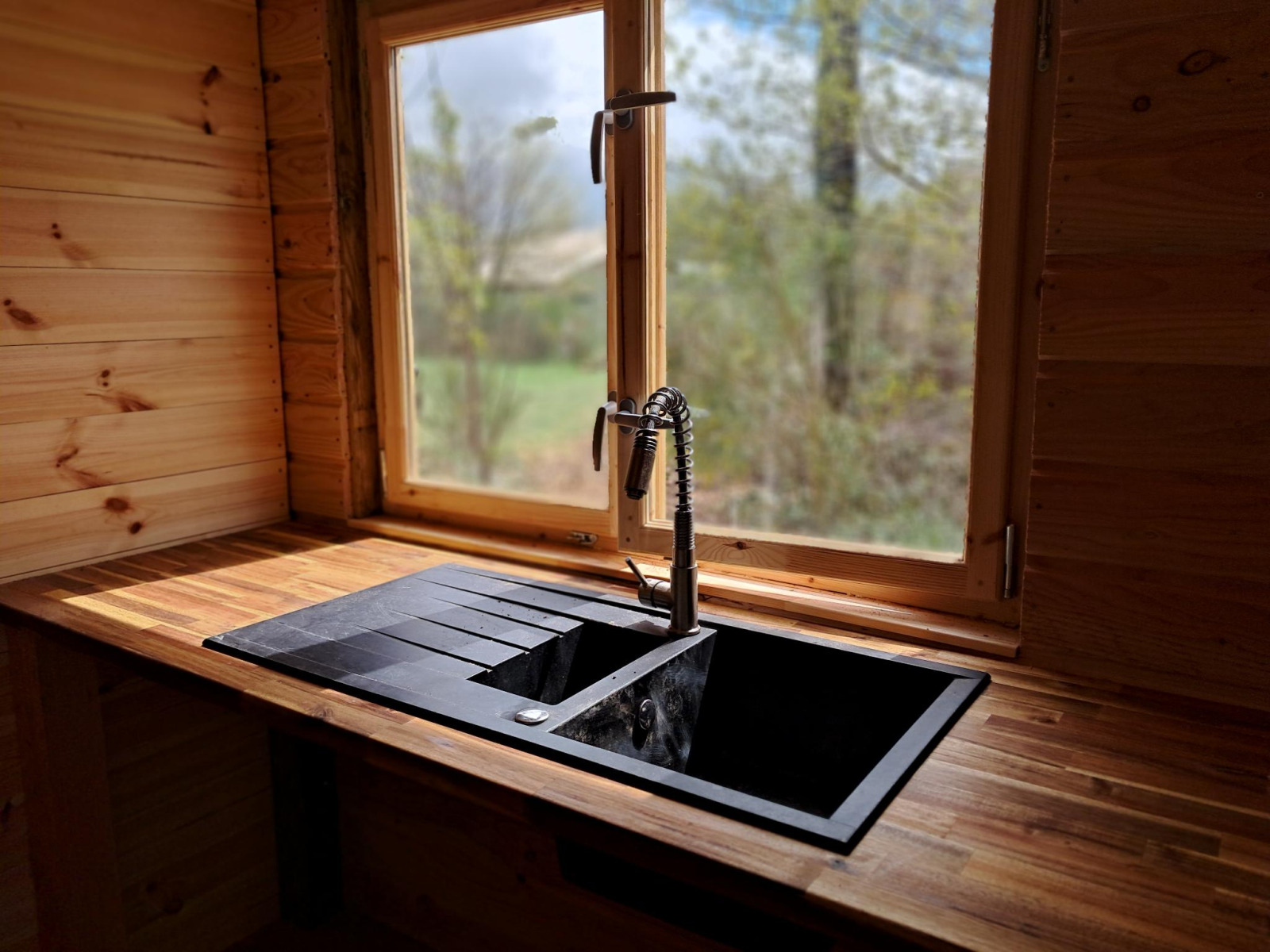 Moderne zwarte keukenkraan en spoelbak bij raam in houten lodge op Camping Junora, Avignon, Frankrijk.