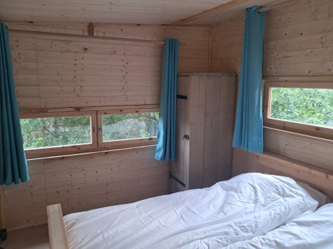 Vista interna di un bungalow in legno con tende azzurre, letto e armadio al camping Junora, Avignone.