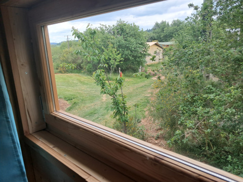 Uitzicht vanuit een raam van lodge 'Avignon' op Camping Junora in Frankrijk, met groen en een pad.