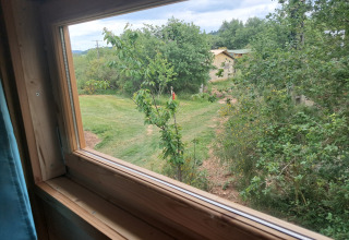 Uitzicht vanuit een raam van lodge 'Avignon' op Camping Junora in Frankrijk, met groen en een pad.